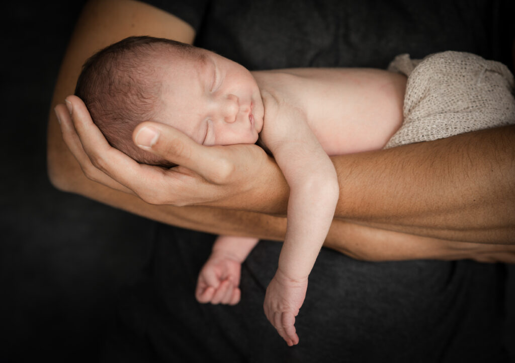 Neugeborenes Baby schläft auf den Händen seindes Papas.