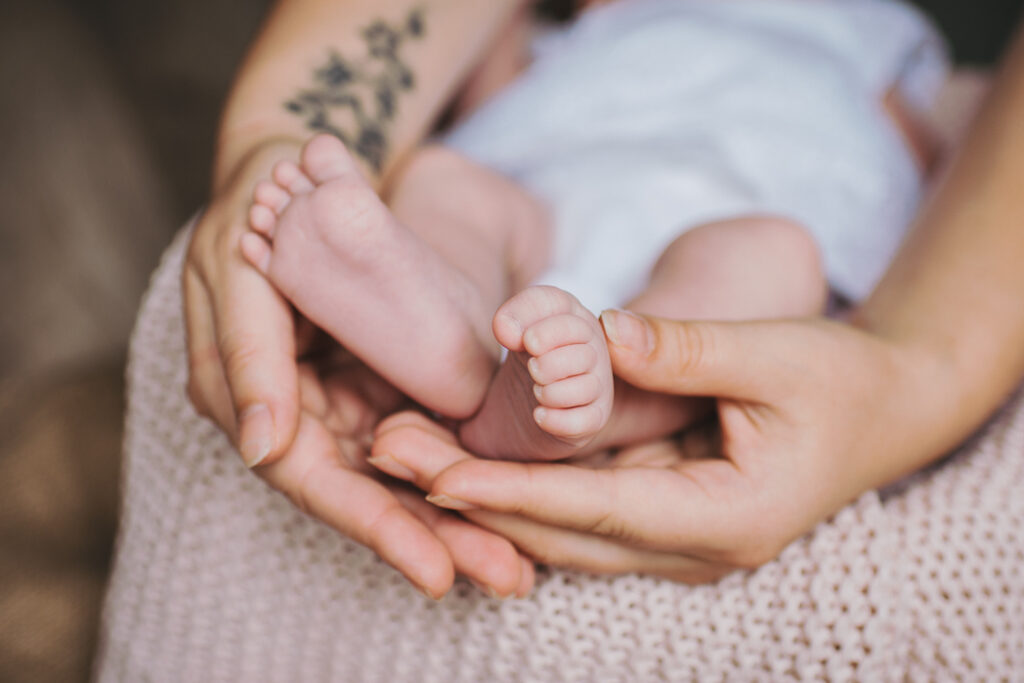 Die Hände einer Frau halten die kleinen Füße ihres neugeborenen Babies.